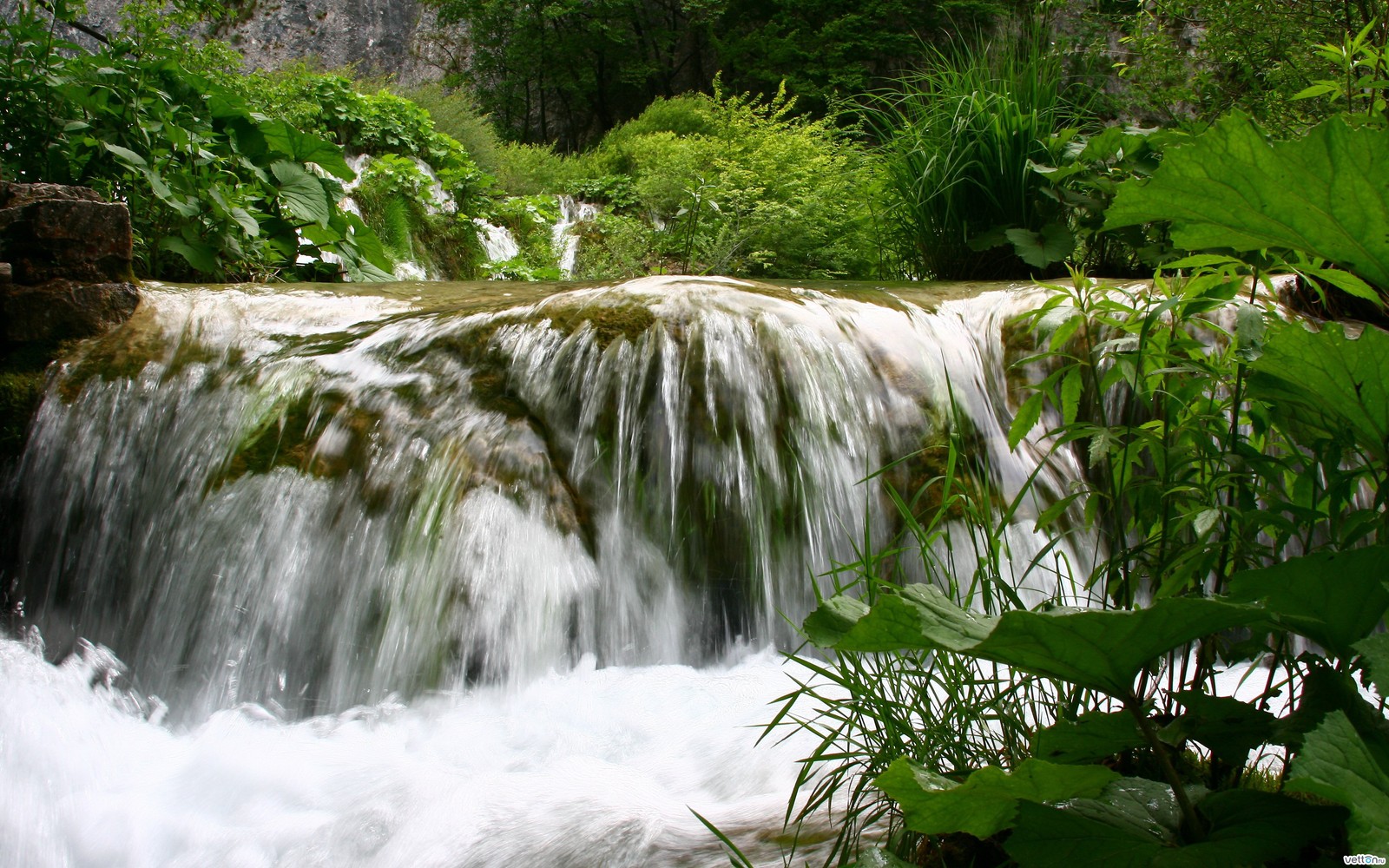 Hay una cascada que fluye por el lado de una montaña (cascada, recursos hídricos, cuerpo de agua, naturaleza, cauce)