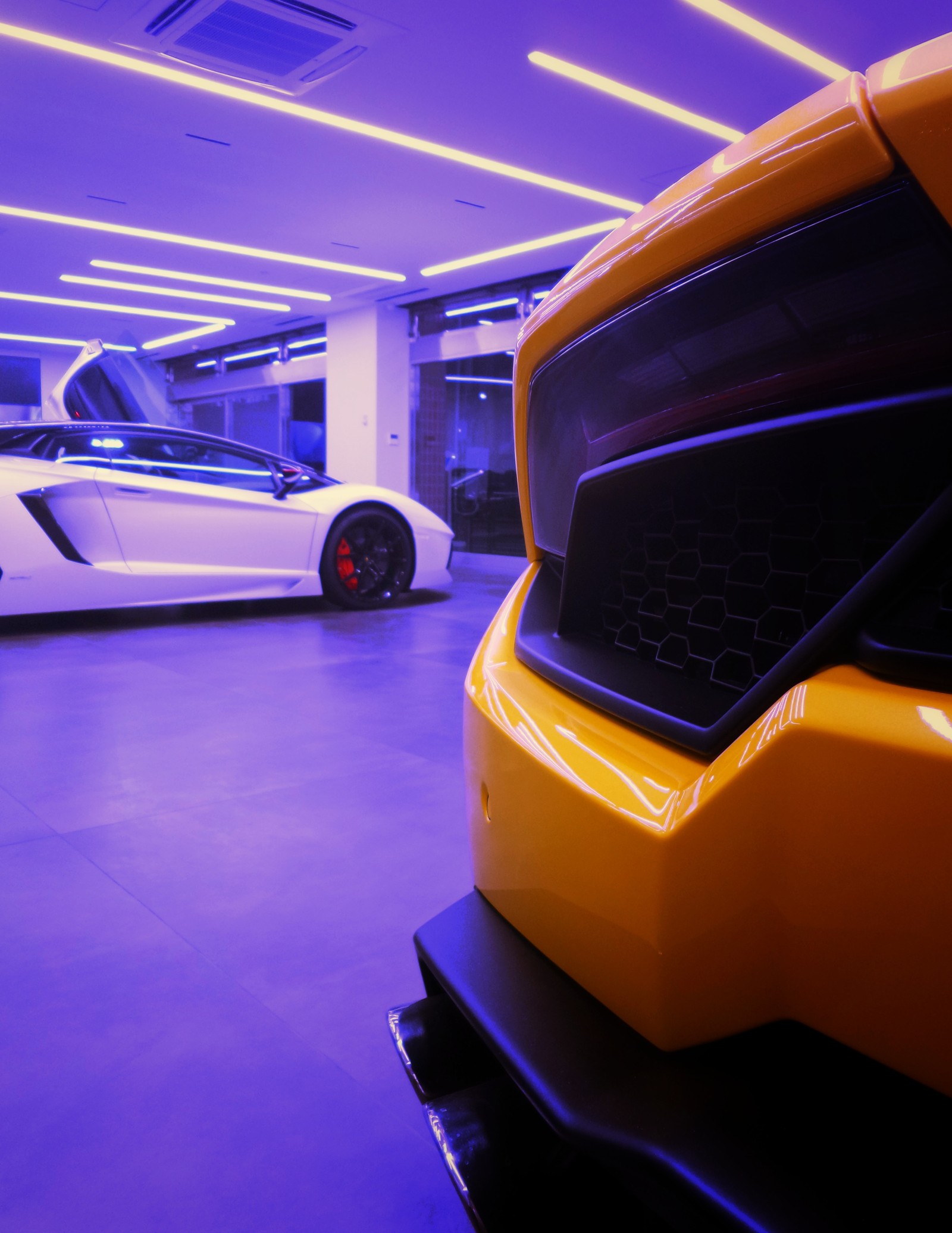 There are two sports cars parked in a garage with purple lighting (sports car, auto show, supercar, automotive lighting, lamborghini)