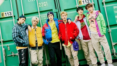 Участники NCT 127 позируют в ярких нарядах на фоне зеленого индустриального пейзажа