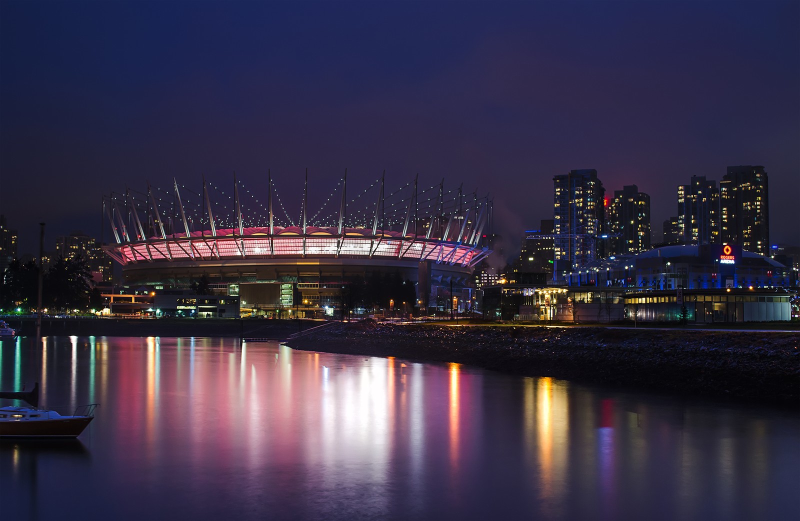 Uma vista aérea de um estádio iluminado à noite com um barco na água (estádio, noite, reflexo, paisagem urbana, marco)