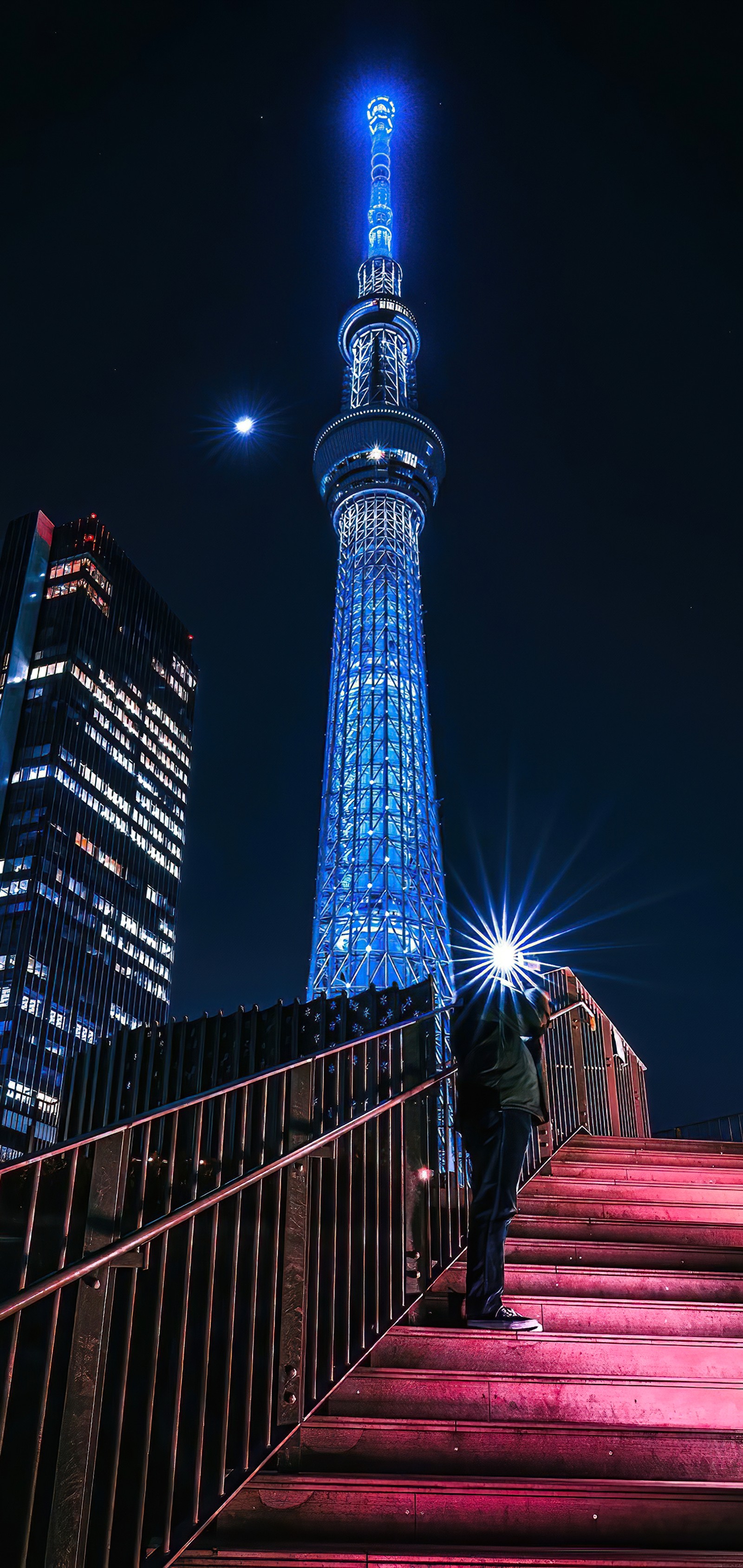 Una vista panorámica de un hombre de pie en un conjunto de escaleras con una torre iluminada al fondo (hito, atracción turística, rascacielos, edificio, torre)