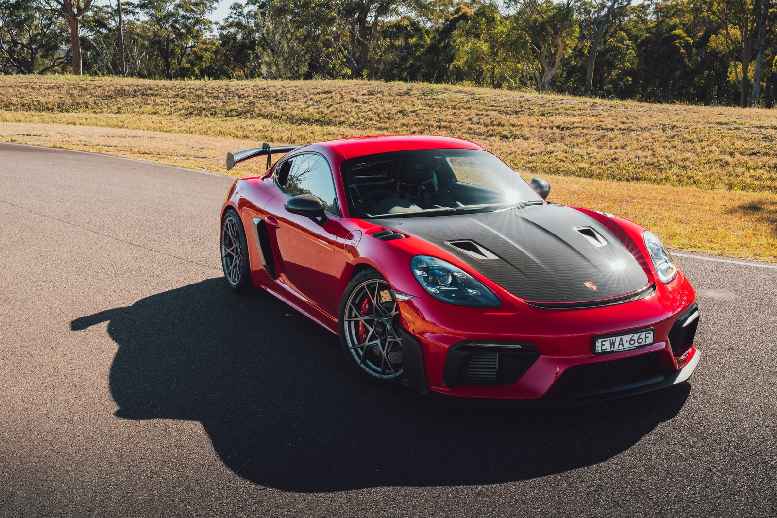 A red porsche sports car driving down a road near a field (porsche 718 cayman gt4 rs, weissach package, 2023, cars, 4k wallpaper)