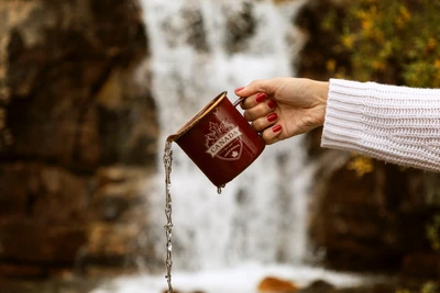 Despejando licor de uma caneca perto de uma cachoeira