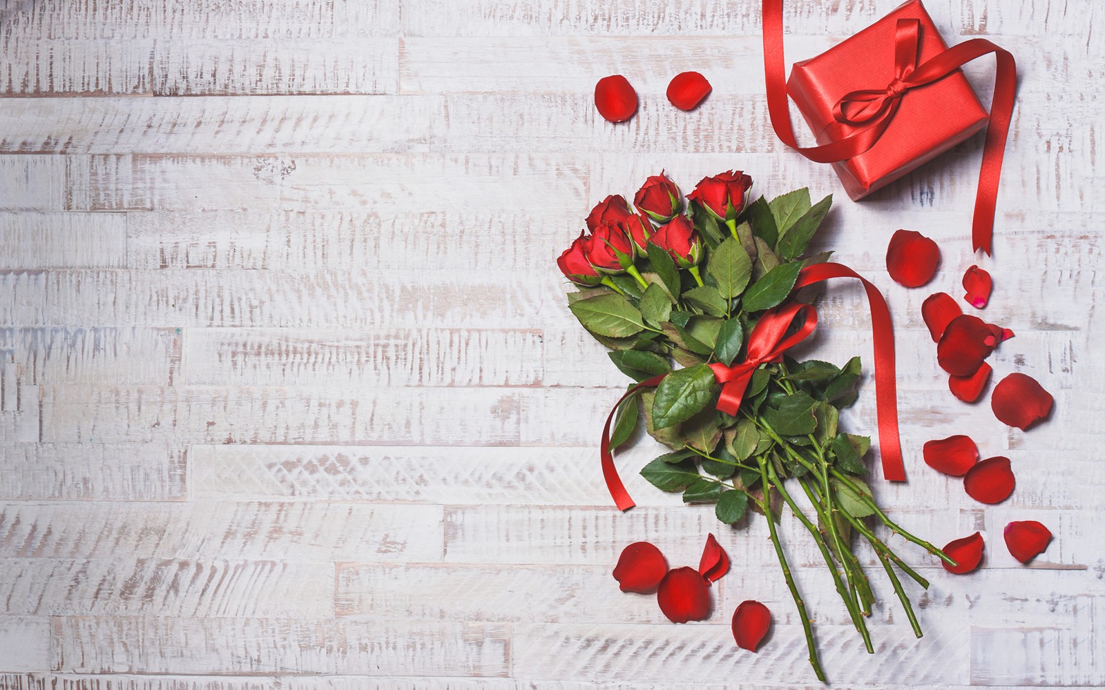 Hay una caja de regalo roja y un ramo de rosas en una mesa de madera blanca (día de san valentín, regalo, flor, diseño floral, amor)