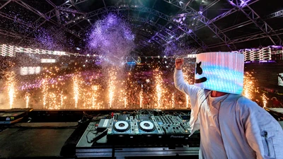 DJ Marshmello actuando en vivo con una multitud vibrante y pirotecnia de fondo.