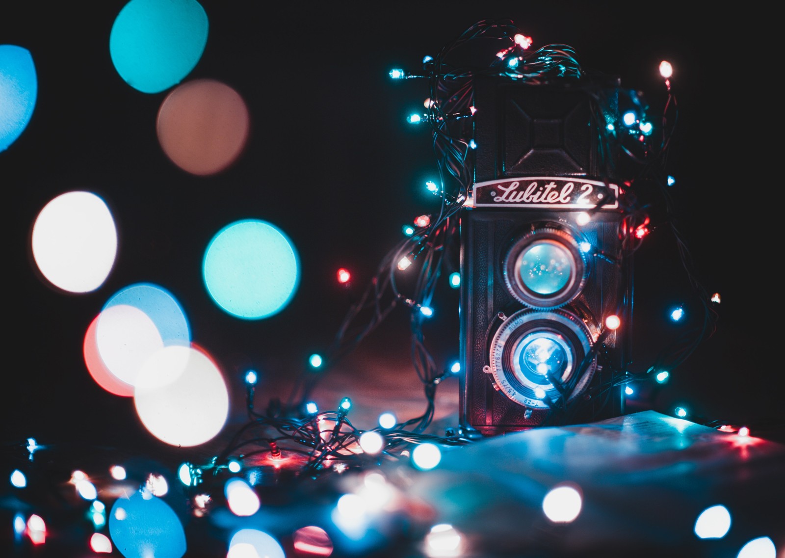 Un gros plan d'une caméra avec une guirlande lumineuse autour. (bokeh, éclairage, lumières de noël, lumière, caméra)