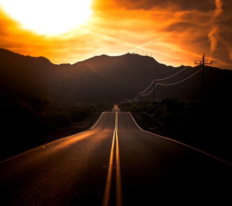 Une vue d'une route avec une montagne en arrière-plan (montagne, coucher de soleil)