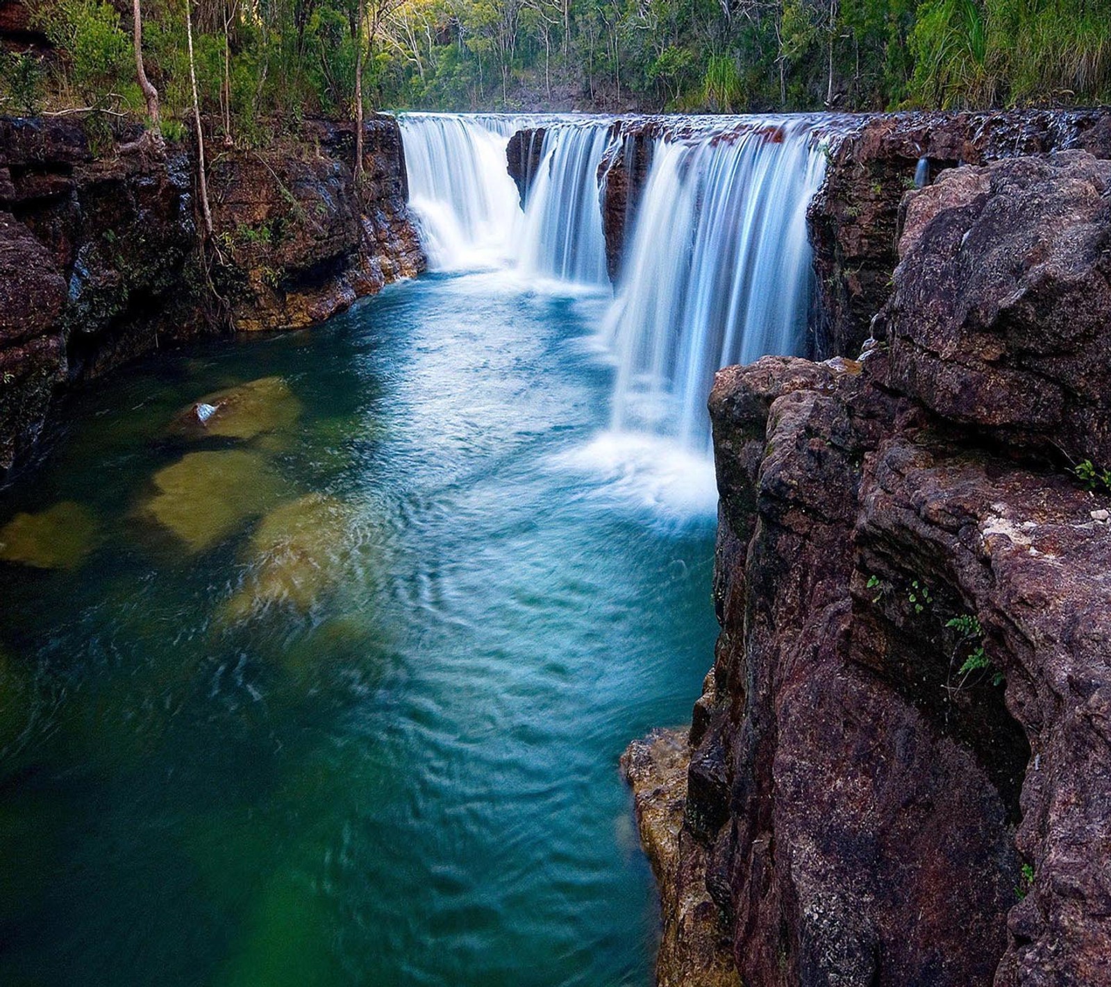 Una cascada artística con una gran cantidad de agua fluyendo sobre rocas (hermoso, lindo, mirada, agradable)