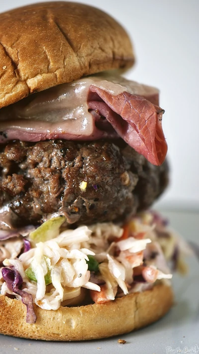 Hamburguesa en capas con carne a la parrilla, queso derretido y una cobertura de ensalada de col rizada en un pan tostado.