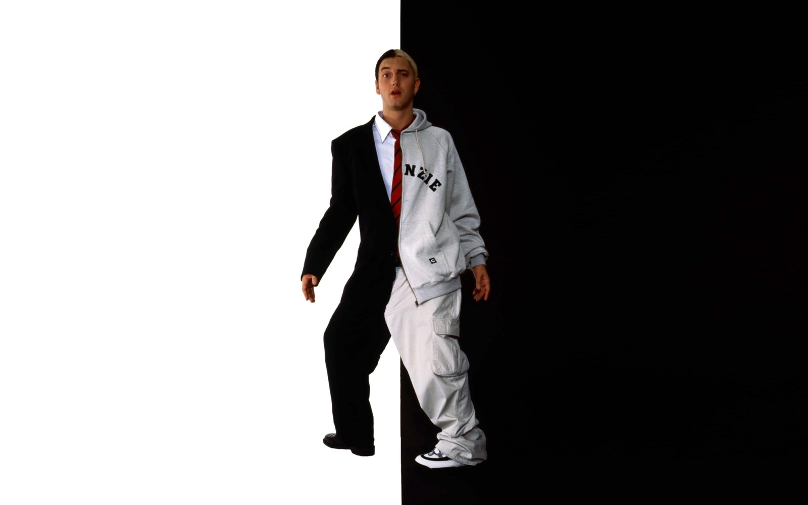 There is a man in a suit and tie standing next to a wall (eminem, formal wear, standing, outerwear, uniform)