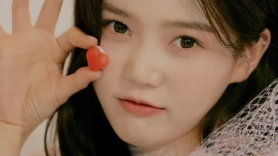 Hyojung von Oh My Girl hält verspielt einen herzförmigen Anhänger nah an ihr Gesicht und strahlt Charme und Wärme aus.