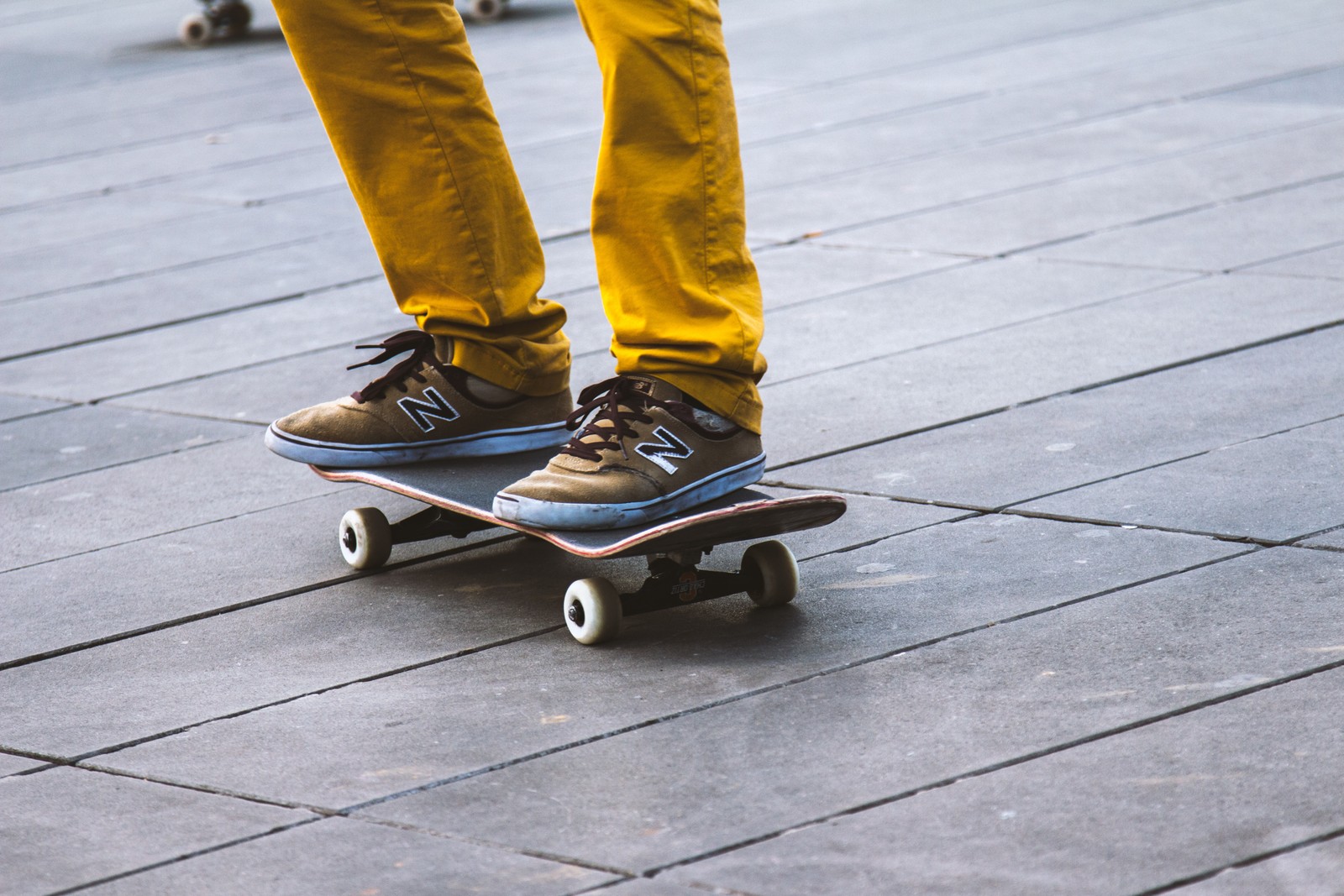 There is a person riding a skateboard on a sidewalk (skateboard, skate shoe, longboard, skateboarding, longboarding)