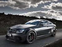 Elegantes Mercedes-Benz C63 AMG Coupé mit auffälligen Leichtmetallrädern vor einem dramatischen Himmel und rustikalem Hintergrund.