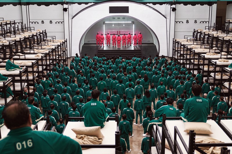 Arafed room with rows of beds and a large group of people in green uniforms (squid game, south korea, netflix, korean drama, entertainment)