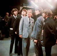 Los Beatles en traje formal con un presentador de televisión en un evento en vivo