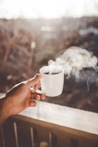 Copo de café fumegante segurado na mão, banhando-se na luz quente do sol.