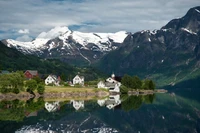 Fjord norueguês sereno com montanhas cobertas de neve e o reflexo de uma charmosa aldeia