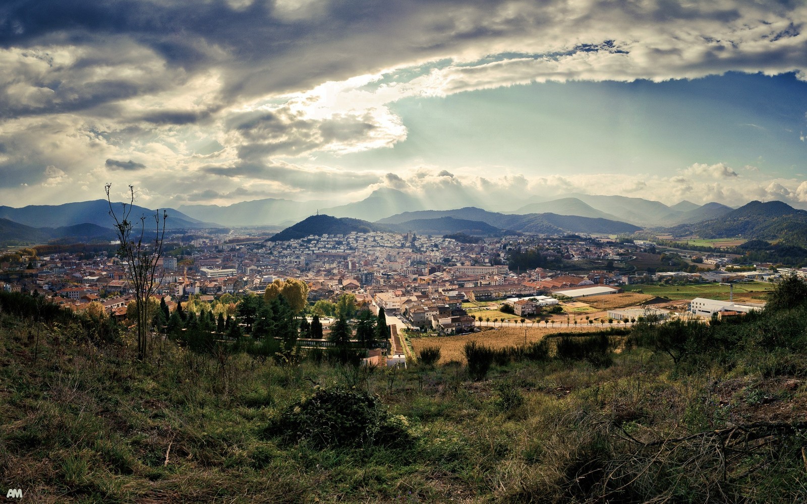 Vue d'une ville depuis une colline avec un ciel nuageux (nuage, formes montagneuses, colline, hauts plateaux, zone rurale)