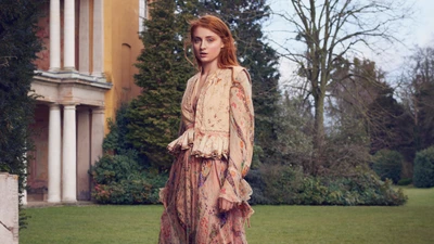 Sansa Stark em um vestido boêmio floral em meio a um cenário de jardim exuberante.