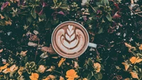 Cappuccino mit kunstvollem Latte-Art, umgeben von lebhaften Blumen.