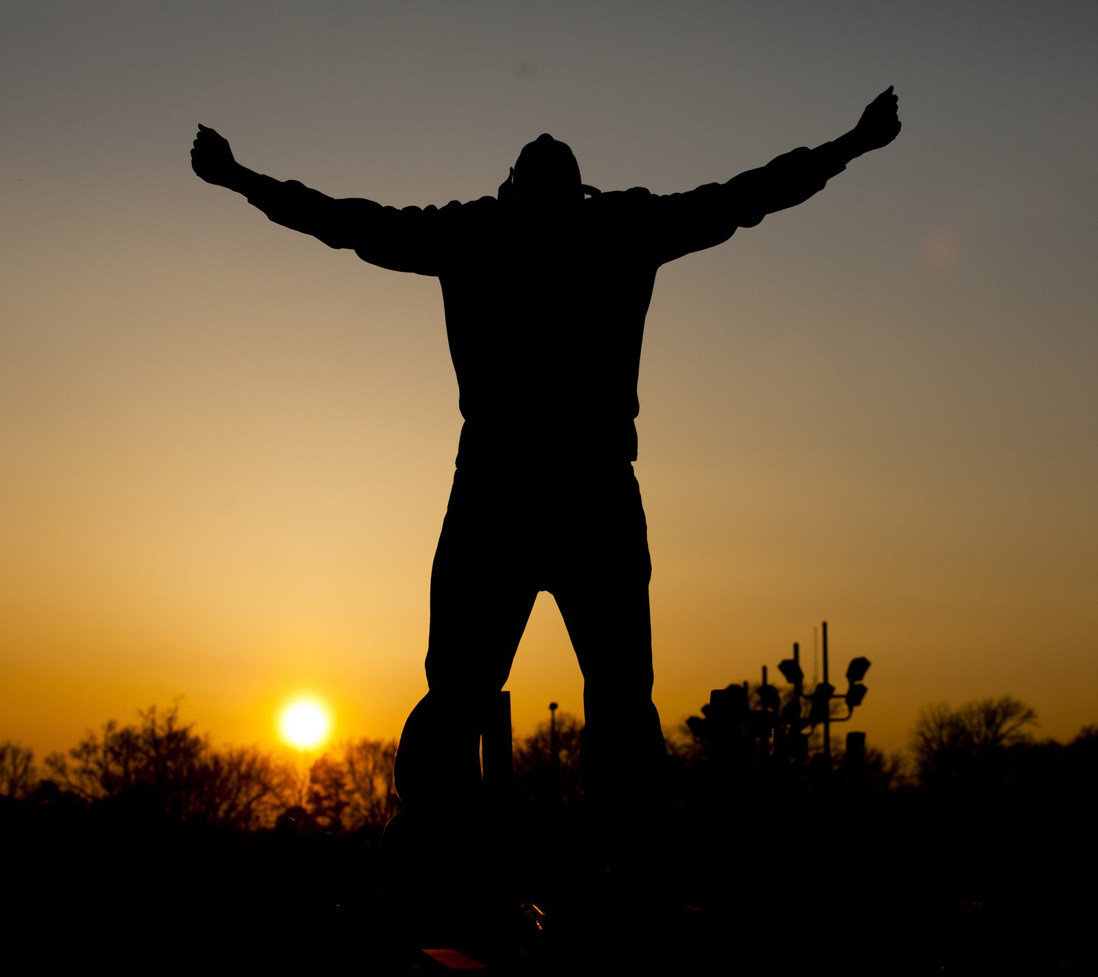 Silhouette d'un homme debout sur un skateboard les bras écartés (ave o, aube, bonjour, lever de soleil, coucher de soleil)