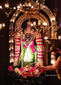 Estatua de la diosa Murugan adornada con flores y rodeada de lámparas de aceite tradicionales.