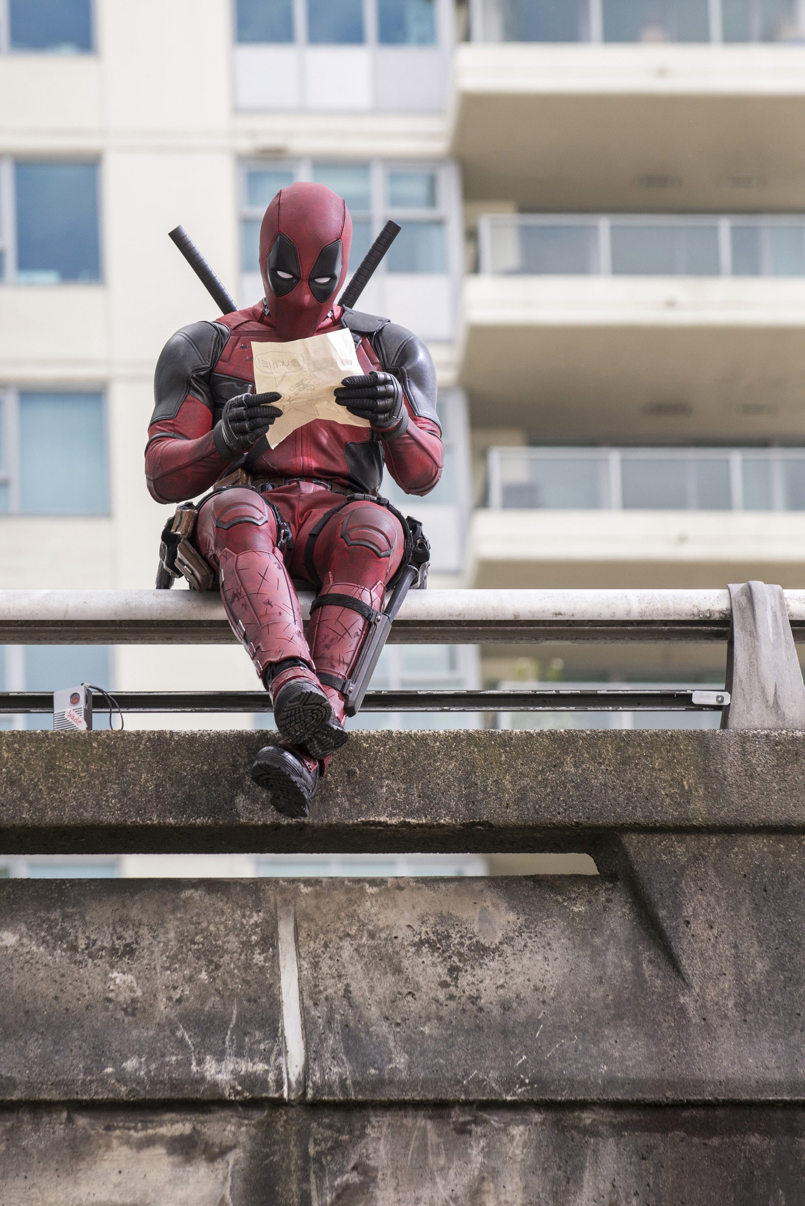 Deadpool assis sur un rebord en train de lire un morceau de papier (hd, marvel, film)