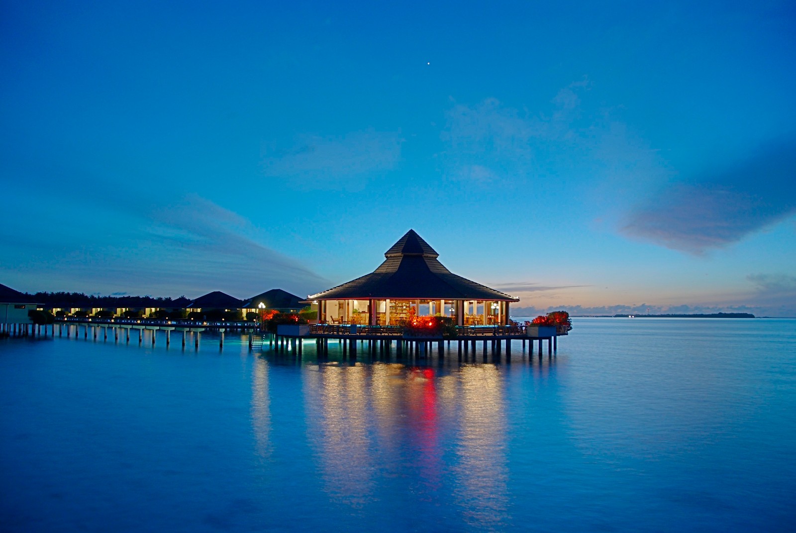 Um edifício em um píer com um telhado de palha e um píer à noite (ilhas maldivas, estância, ilha, ilha resort, azul)