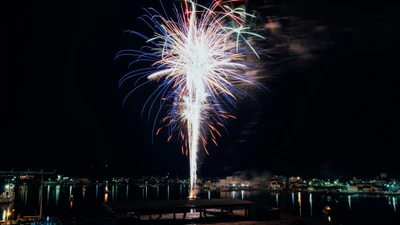 Fogos de artifício vibrantes iluminam o céu noturno sobre uma celebração festiva à beira-mar