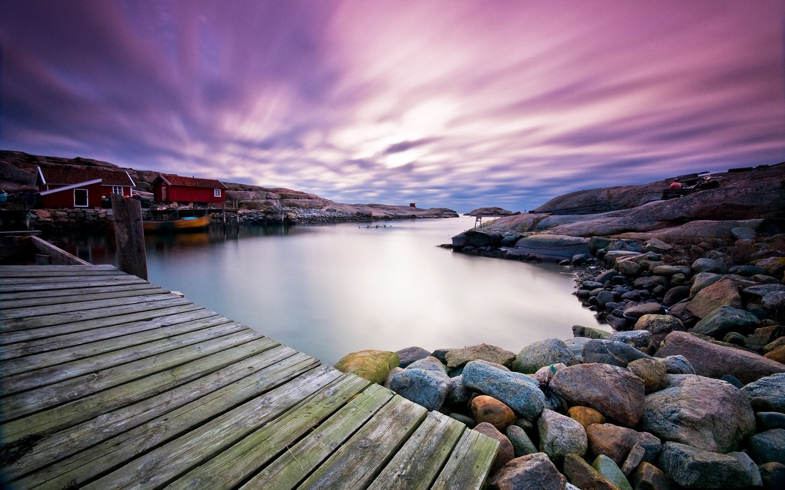 A wooden dock with rocks and a boat on the water (water, cloud, morning, sea, macbook pro)