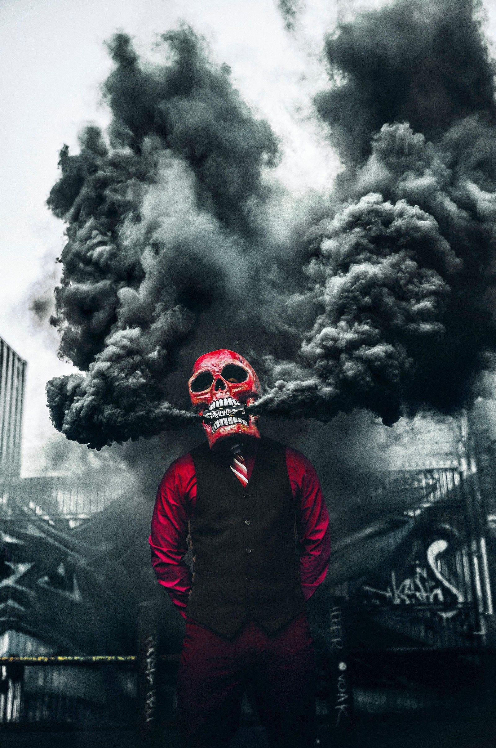 There is a man with a mask and a vest standing in front of a smoke filled city (mask, skull, smoke bomb, smokebomb)