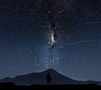 Starry night sky illuminating a lone figure against a mountain backdrop.