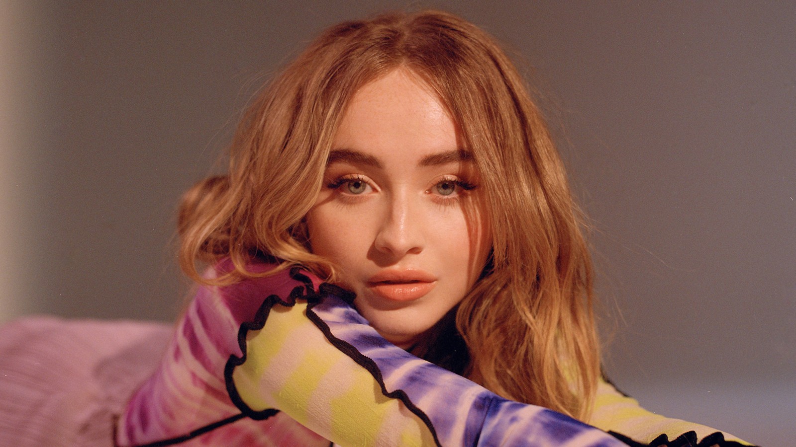 Una imagen borrosa de una mujer acostada en una cama con una camisa colorida (sabrina carpenter, cantante, celebridad, chicas, sesión de fotos)