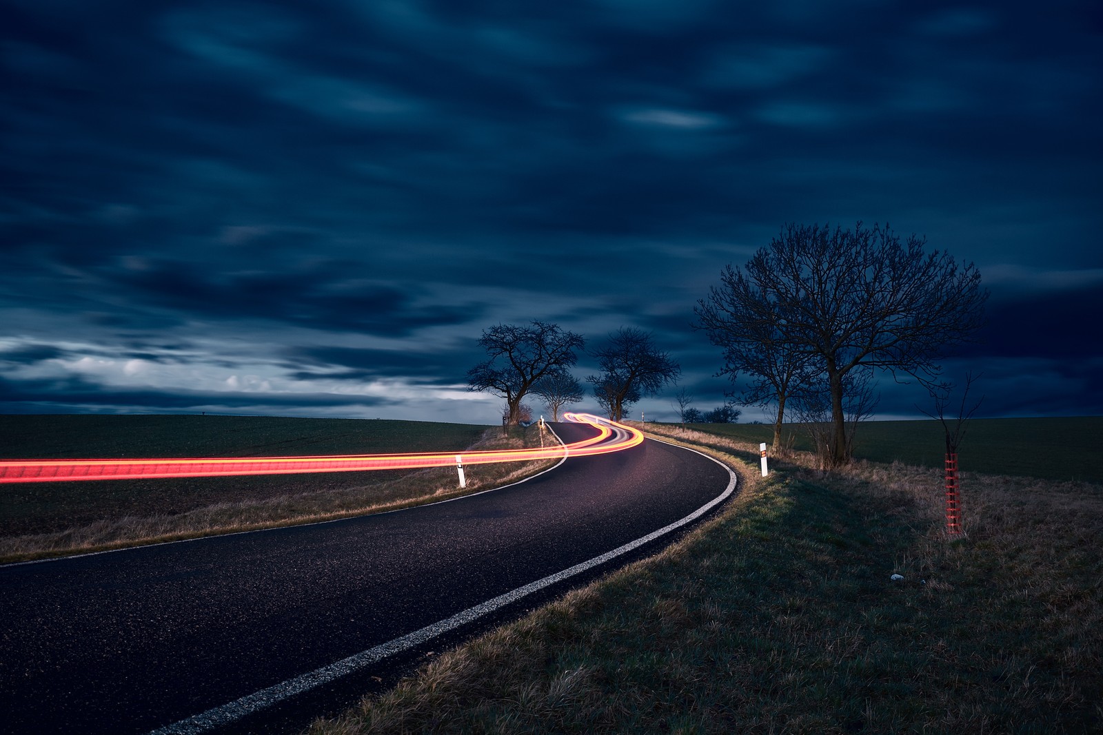 Arafed view of a road with a car passing by on a cloudy night (road, night, blue, cloud, tree)