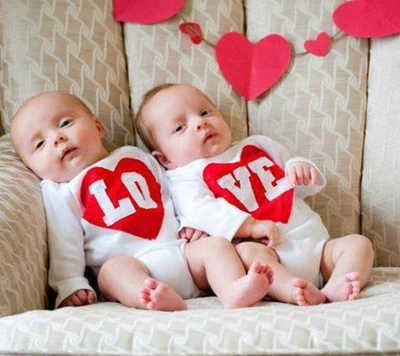 Adorable twins in matching outfits with red heart designs, embodying love.