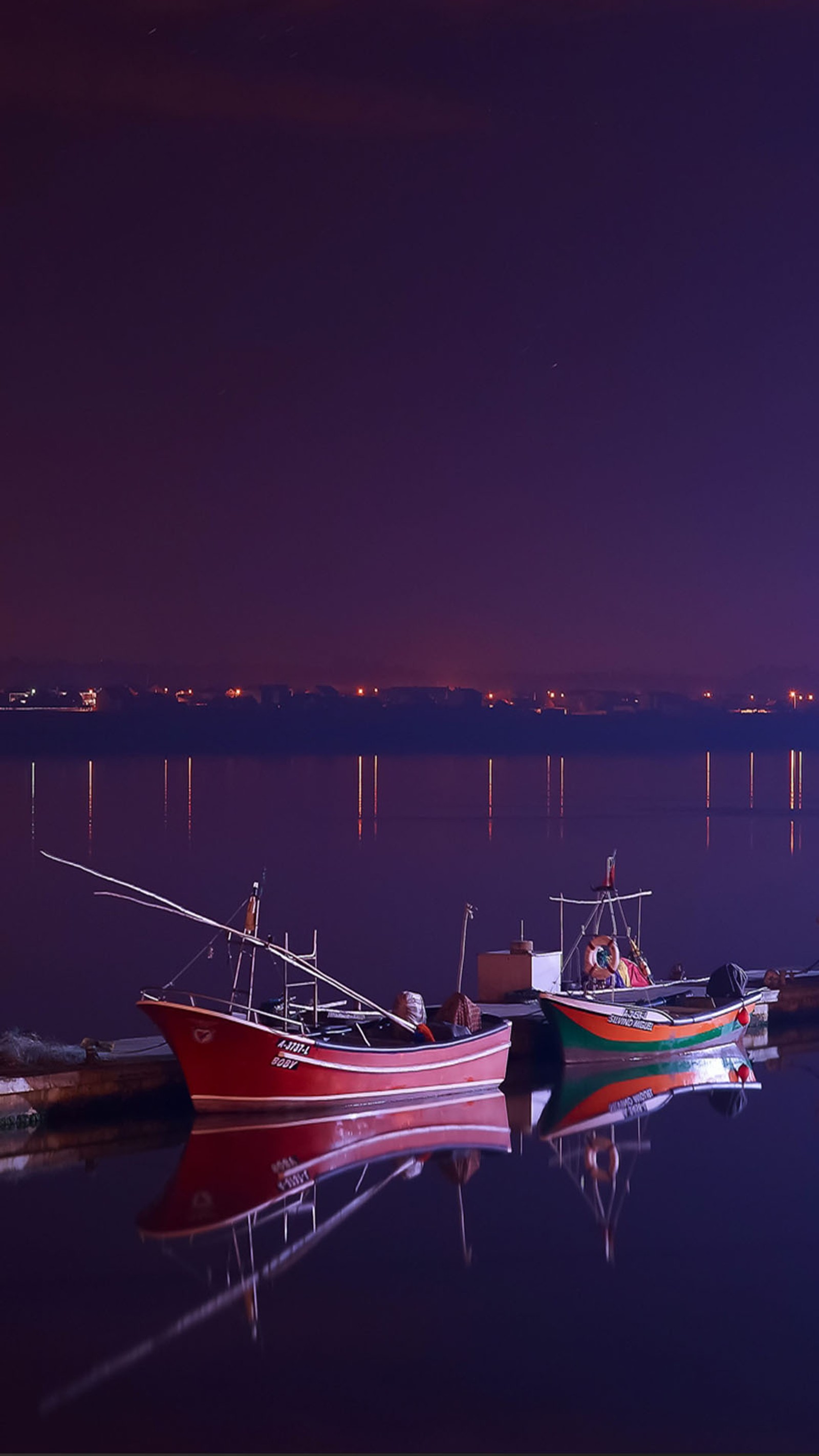 Barcos atracados em um cais à noite com uma cidade ao fundo (barcos, água)