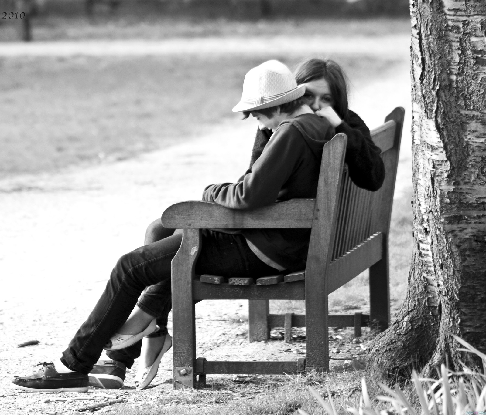 Il y a un homme et une femme assis sur un banc à côté d'un arbre (couple, mignon, amour, romantique, arbre)