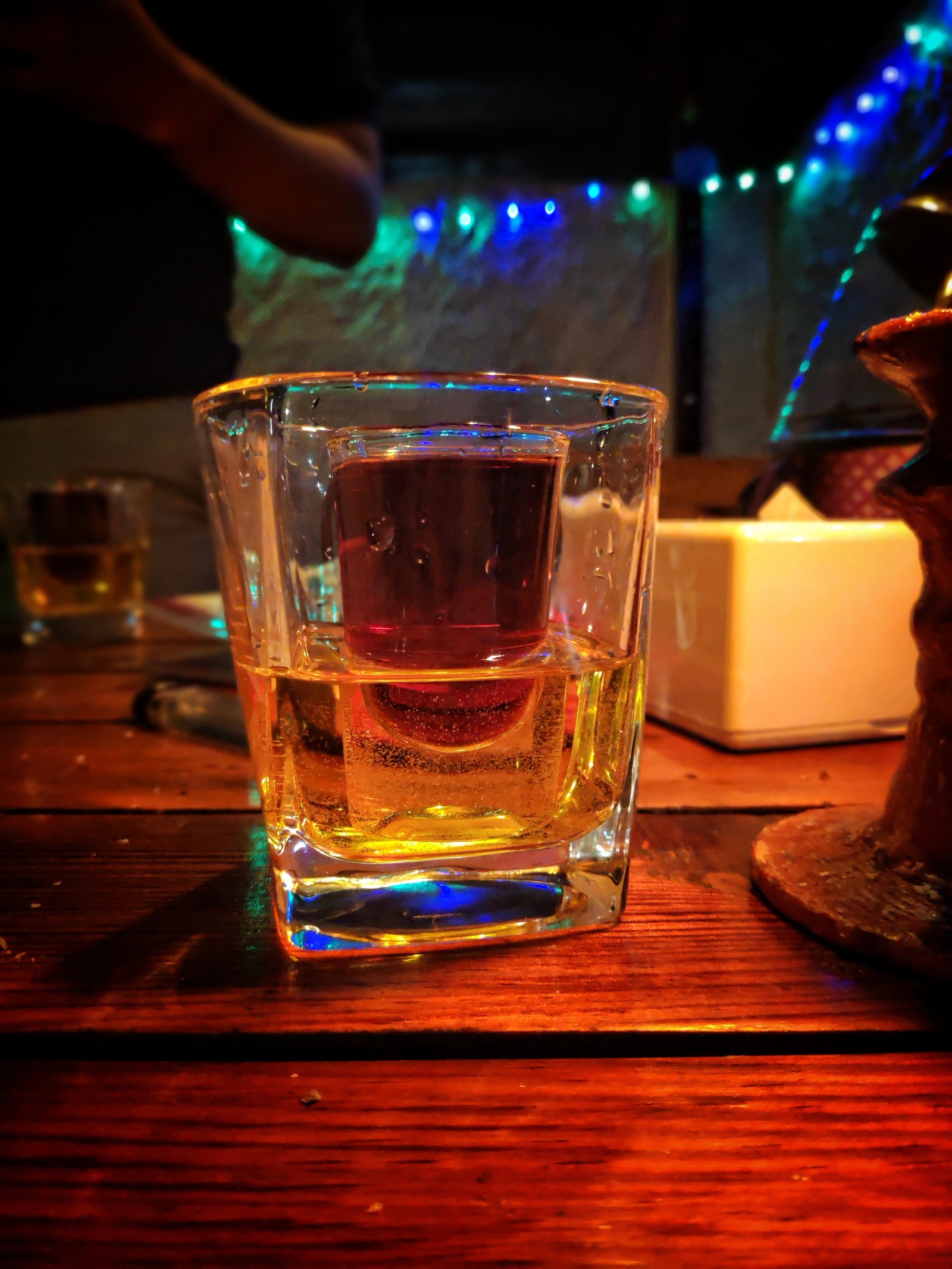 There is a glass of alcohol sitting on a table with a candle (jagerbomb, whiskey, cocktail, redbull, alcohol)