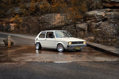 Volkswagen Golf clássico estacionado em uma estrada cênica com rochas íngremes ao fundo.