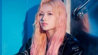 Minatozaki Sana de TWICE con cabello rosa, exudando confianza en una elegante chaqueta de cuero negra contra un vibrante fondo azul.