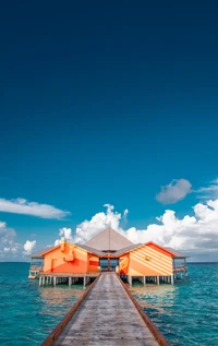 Bungalow sur pilotis orange vif contre un océan turquoise sous un ciel dégagé