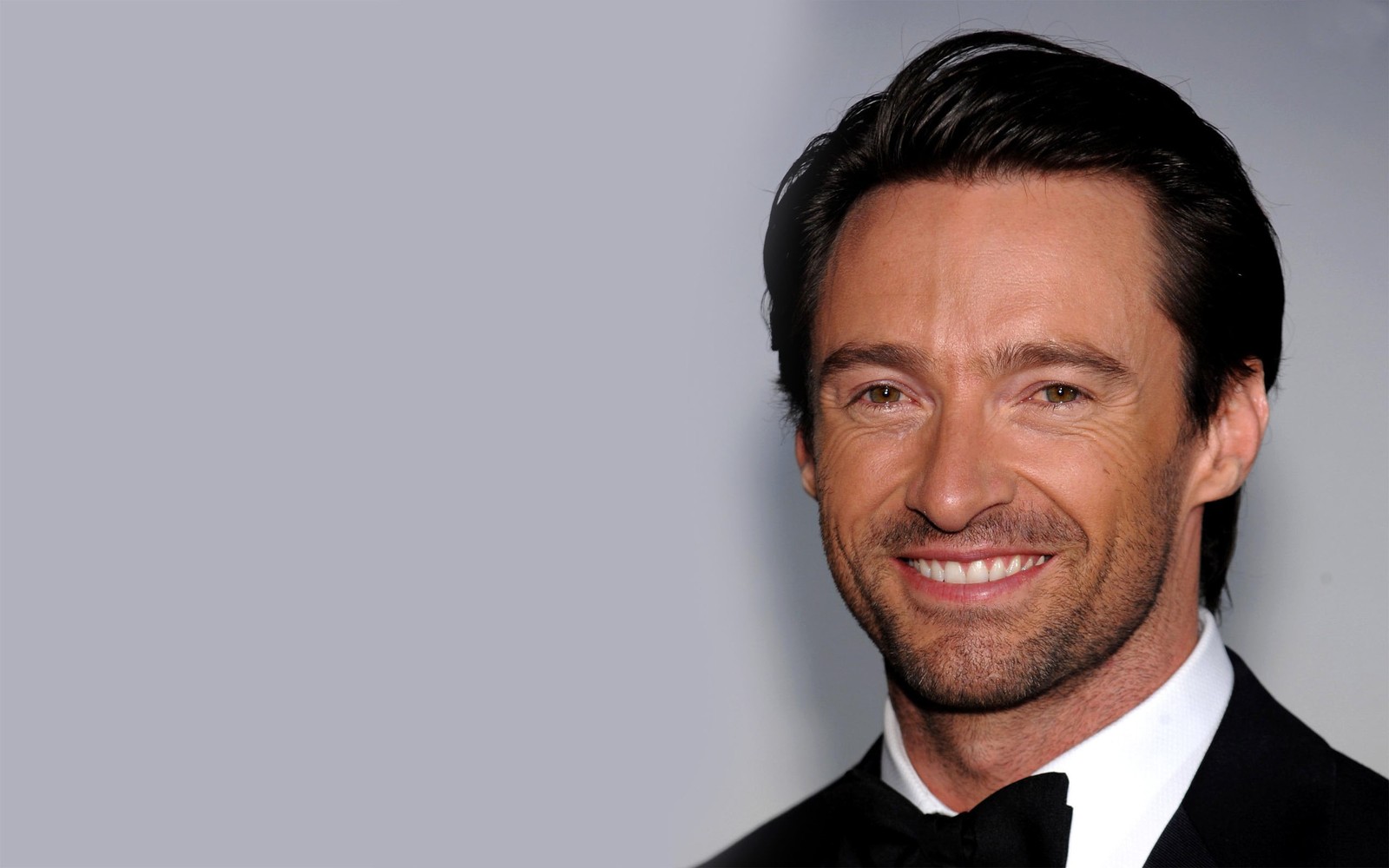 Un primer plano de un hombre en esmoquin sonriendo a la cámara (hugh jackman, wolverine, mentón, frente, vello facial)