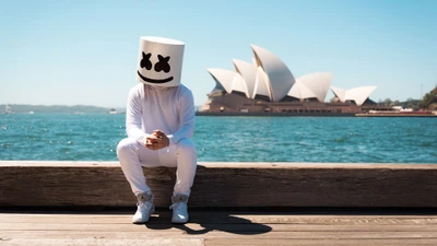 Marshmello sentado junto al agua con la Ópera de Sídney de fondo.