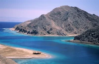 Vista costeira de tirar o fôlego da Península do Sinai com uma baía serena, praia de areia e montanhas acidentadas contra um céu azul claro.