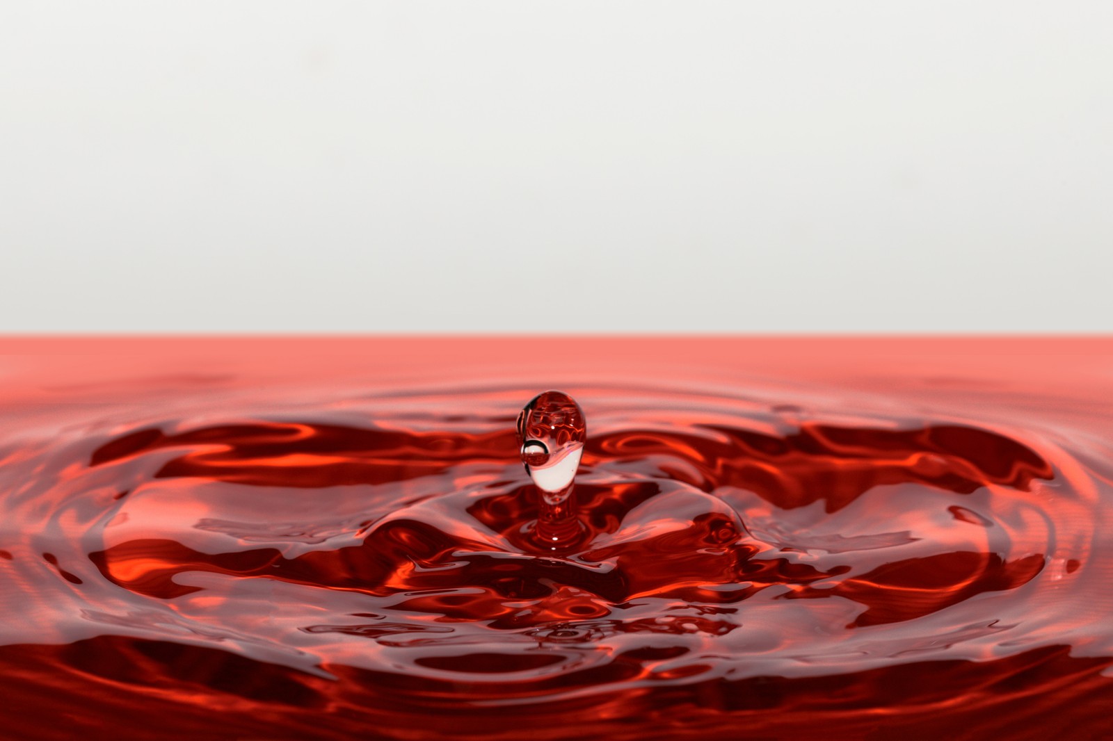 Um close de uma gota de líquido vermelho em um fundo branco (vermelho, onda, líquido, água, gota)