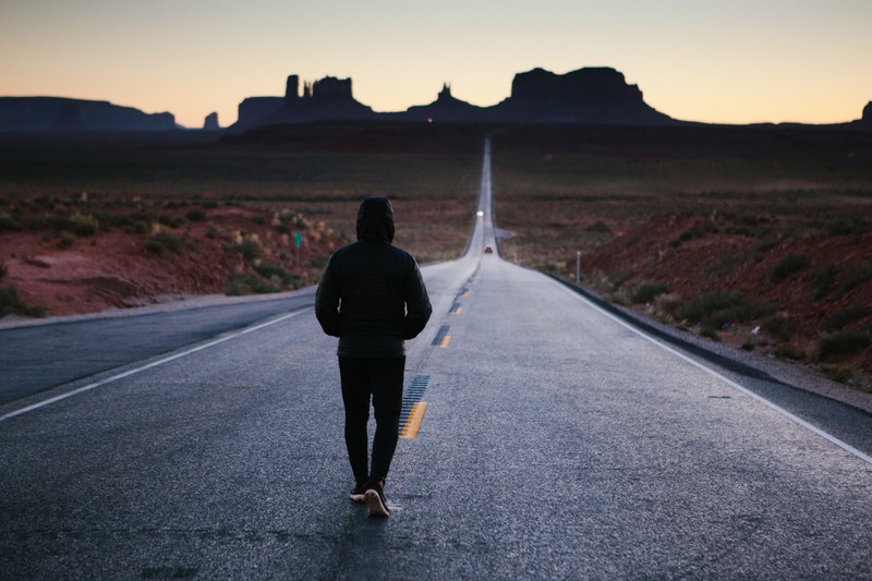 Арафедный мужчина идет по дороге посреди пустыни (долина памятников, monument valley, дорога, горизонт, пейзаж)