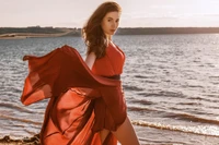 Mujer elegante con vestido rojo junto al mar al atardecer