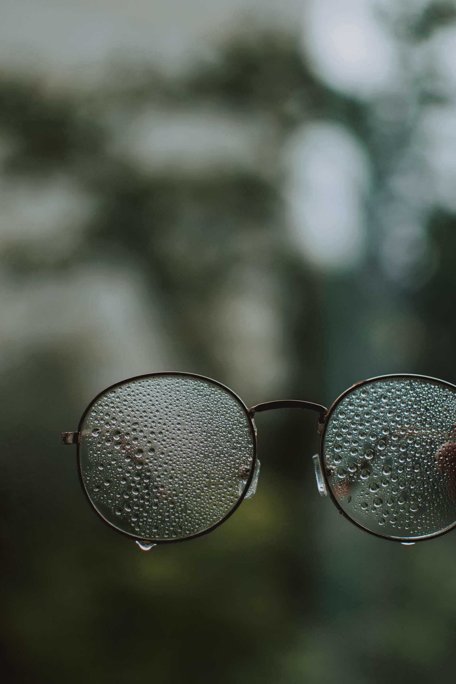 Someone holding a pair of glasses with water droplets on them (glasses, eyewear, audio equipment, paper, close up)