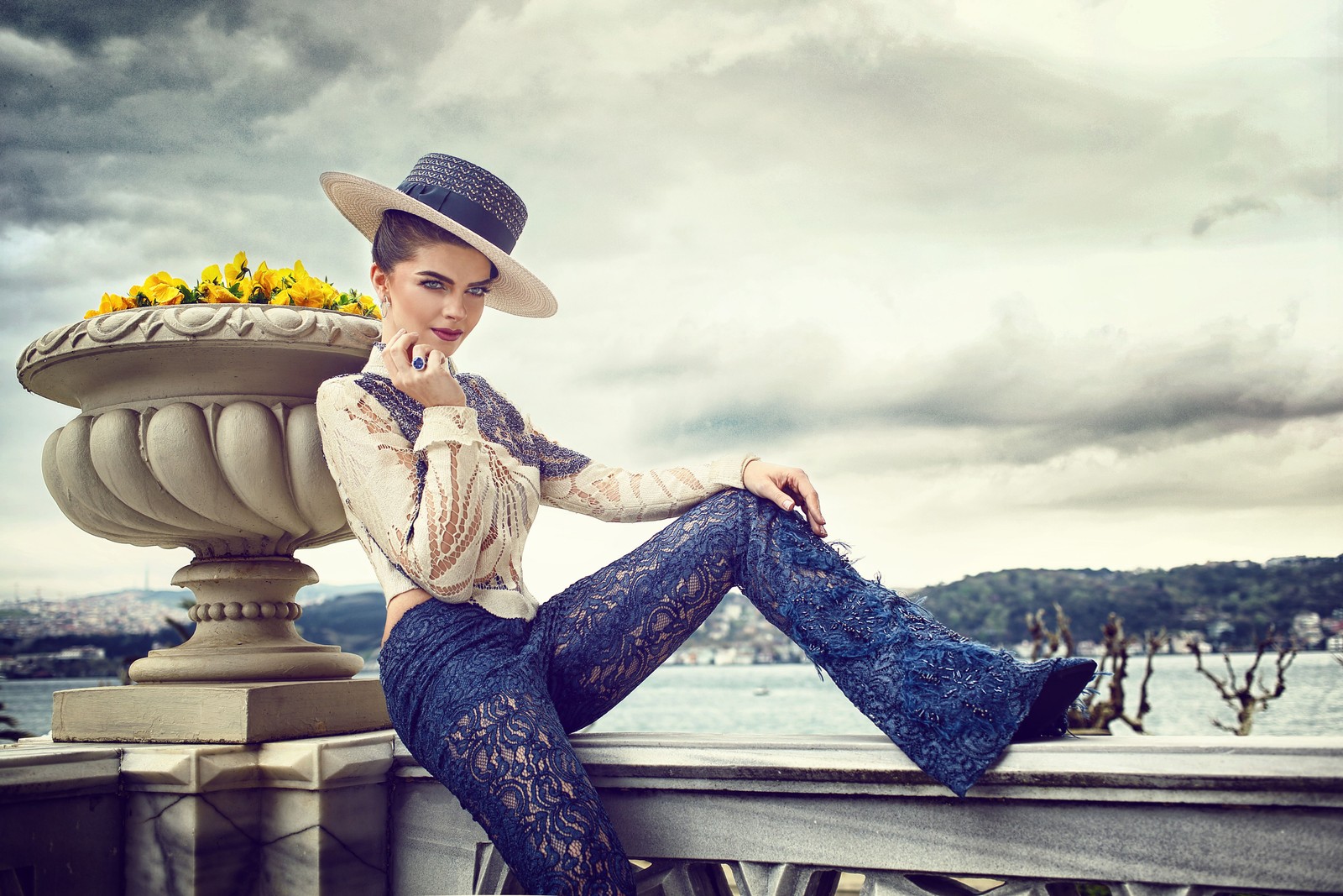 Une femme assise sur une rambarde avec un chapeau et un pot de fleurs (acteur, jeans, beauté, mode, assis)