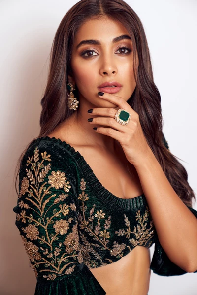 Retrato elegante de Pooja Hegde, exibindo bordados intrincados em um traje verde escuro, complementado por joias statement.